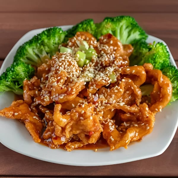 Sesame chicken with broccoli florets and green onions on a white plate from Wang Chinese Restaurant.