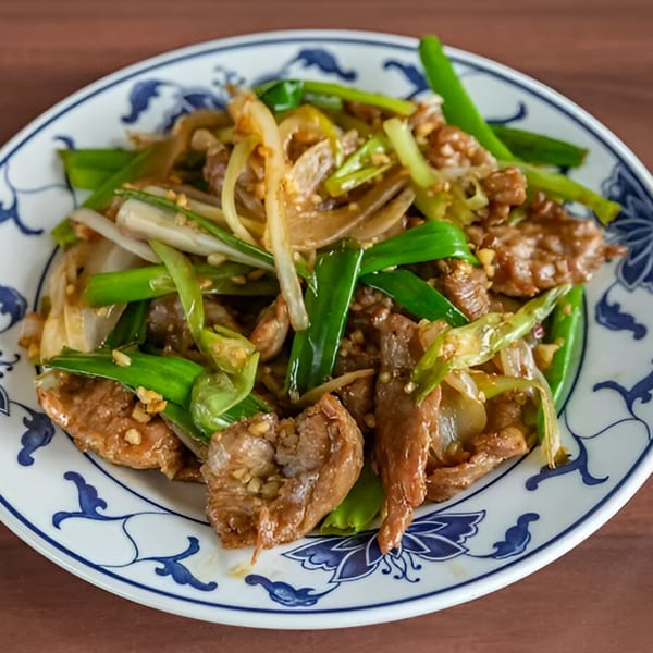 A close-up of a Chinese stir-fry dish with beef, green onions, and white onions on a patterned plate.