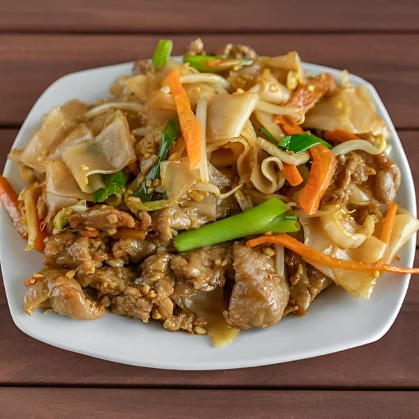 Close-up of Chinese beef chow fun with wide noodles, carrots, and green onions.