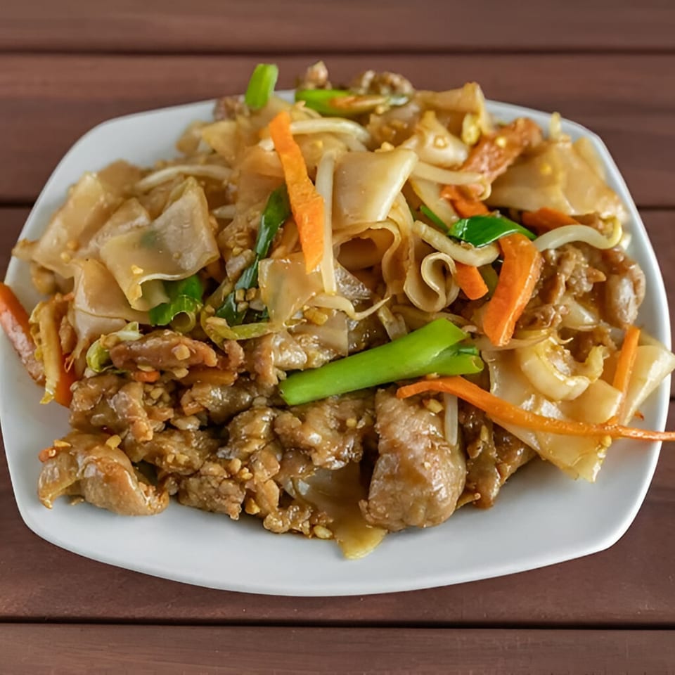 Close-up of Chinese beef chow fun with wide noodles, carrots, and green onions.