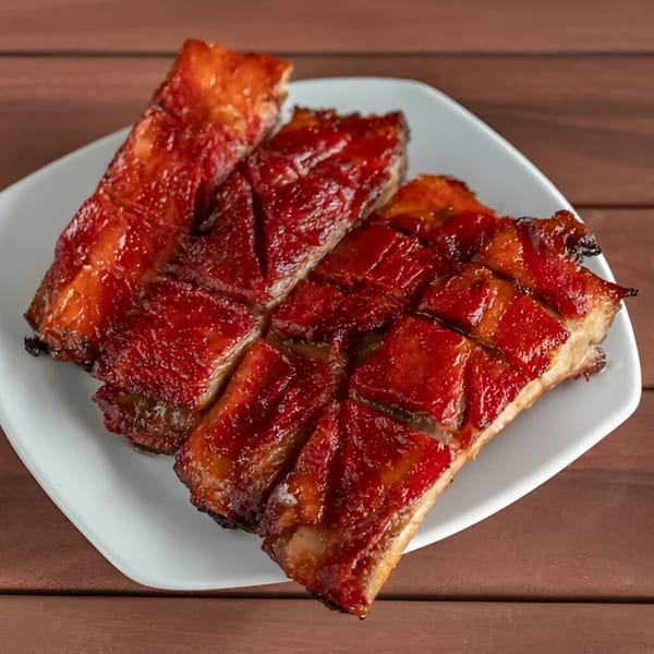 Close-up of glistening, sliced char siu (Chinese BBQ pork) on a white plate.